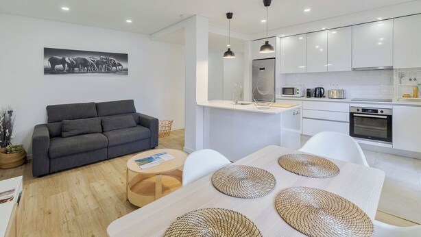 A modern living room with a grey sofa, a coffee table, and a dining table with woven placemats. - Fonte Nova Nest (Sesimbra)