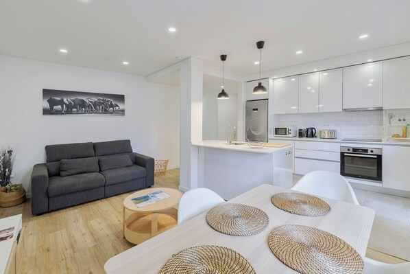 A modern living room with a grey sofa, a coffee table, and a dining table with woven placemats.
