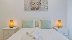 A neatly made bed with white linens, two bedside tables with lamps, and a wall-mounted artwork above the bed. - Fonte Nova Nest (Sesimbra)