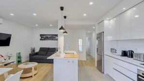 A modern kitchen with white cabinets, a central island, and a dining area with a table and chairs. - Fonte Nova Nest (Sesimbra)