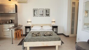 Een moderne slaapkamer met een groot bed, nachtkastjes, een kleine keuken en een badkamer door een open deur.