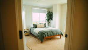 Un dormitorio con cama, un tapete redondo tejido, una planta en maceta y una ventana.