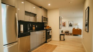A modern kitchen with stainless steel appliances, a microwave, and a dining area with a sofa and table. - Chic Cozy Retreat - 2BR - Stunning North End Views (Halifax)