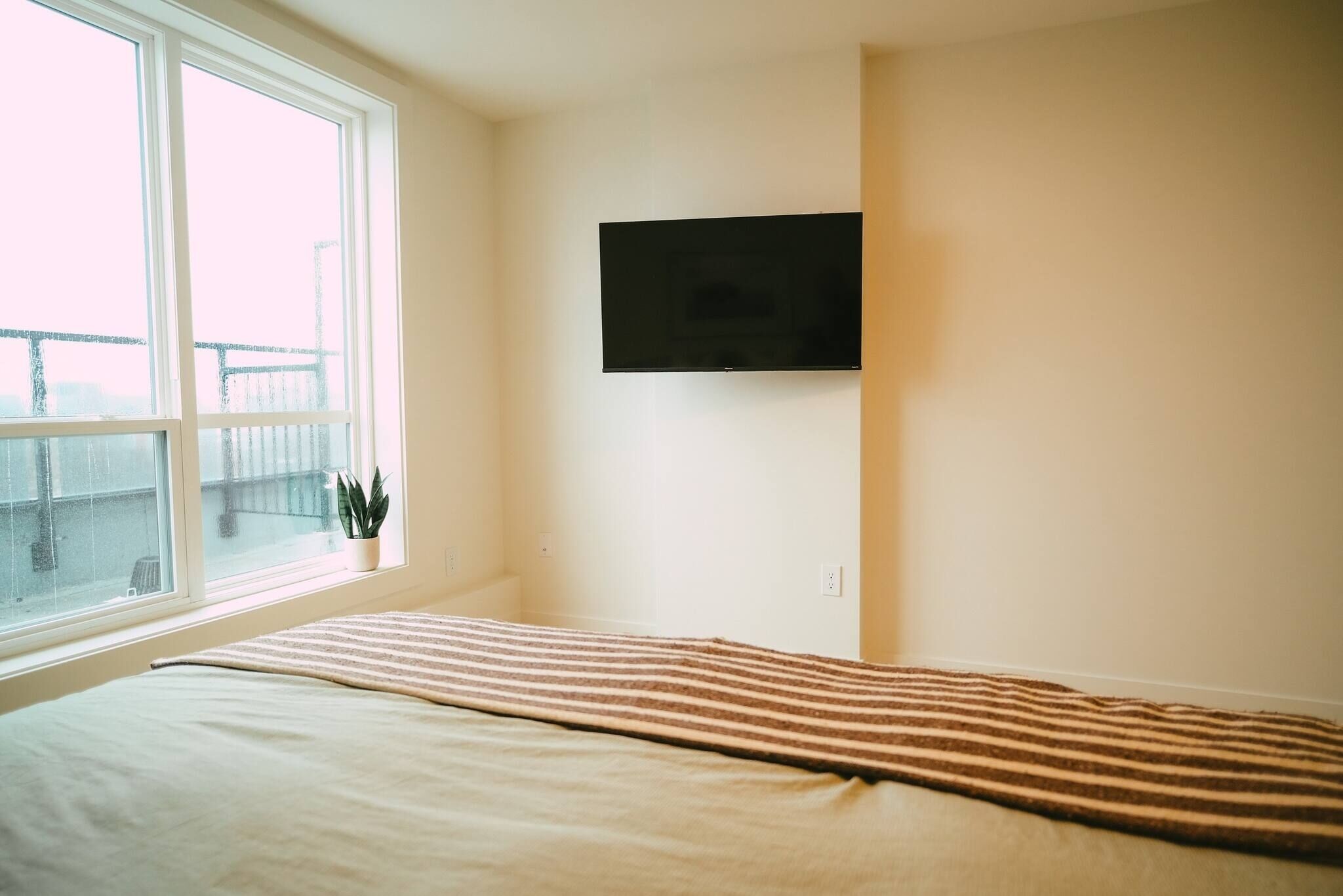 A bedroom with a bed, a window with a view, and a mounted TV.