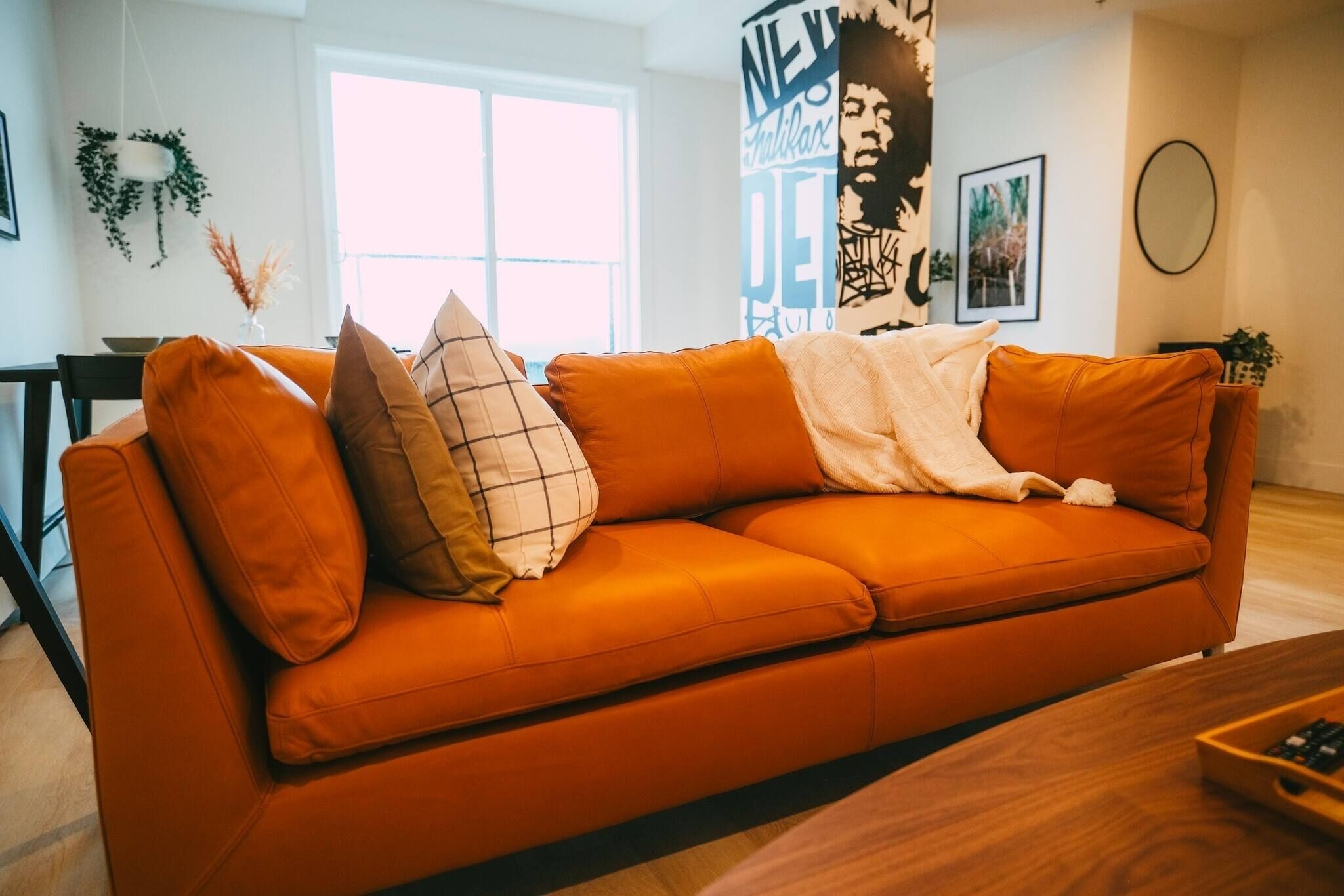 A modern living room with a large orange sofa, a wooden coffee table, and a large window providing natural light.