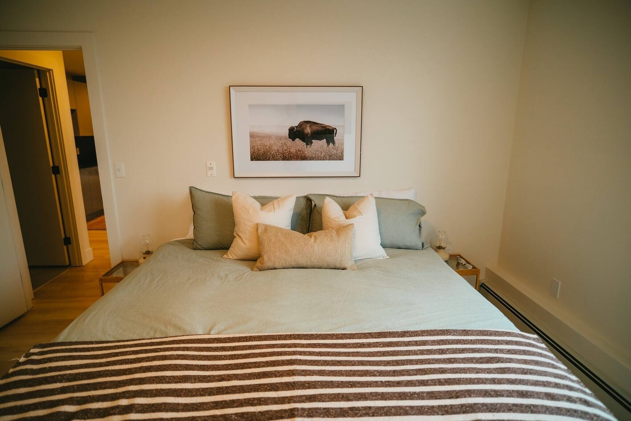 A bedroom with a bed, pillows, a framed picture on the wall, and a striped blanket.