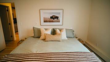 A bedroom with a bed, pillows, a framed picture on the wall, and a striped blanket.