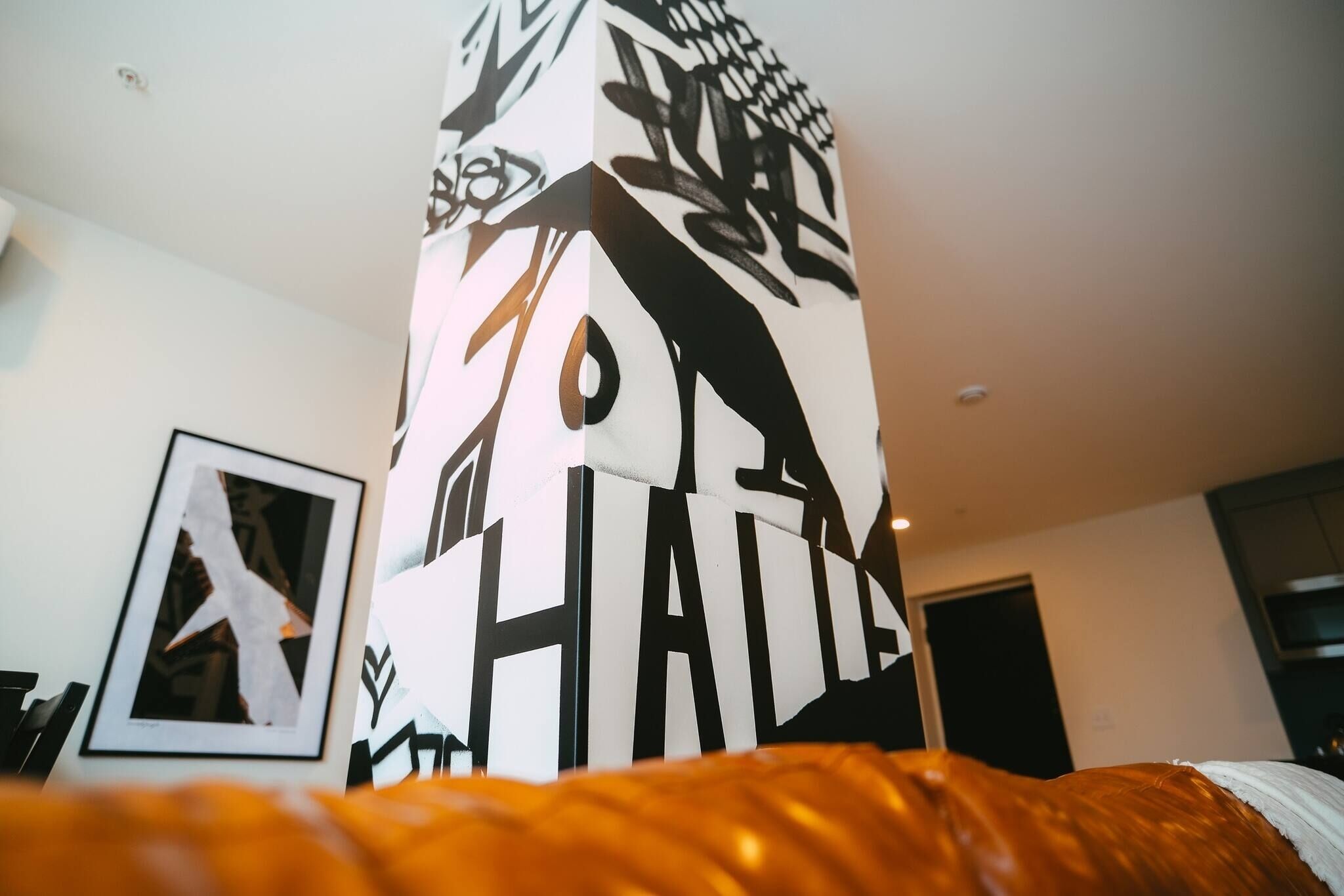 A room with a bed, a framed picture on the wall, and a tall, narrow column with abstract designs.