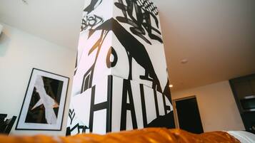 A room with a bed, a framed picture on the wall, and a tall, narrow column with abstract designs.