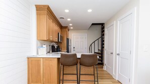 A kitchen with wooden cabinets, a white countertop, two bar stools, and a white door in the background. - North OC-short walk 2 beach & Park (Ocean City)