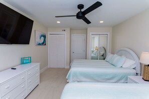 Un dormitorio con dos camas, ventilador de techo, televisor, cómoda y espejo.