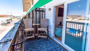 A balcony with chairs and a table, a view of the street, and a building with a green awning. - North OC-short walk 2 beach & Park (Ocean City)