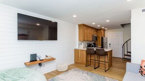 A modern kitchen with wooden cabinets, a bar stool, and a flat-screen TV mounted on the wall. - North OC-short walk 2 beach & Park (Ocean City)