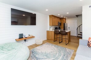 A modern kitchen with wooden cabinets, a bar stool, and a flat-screen TV mounted on the wall.