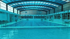 Una piscina interna con tetto in vetro, acqua cristallina e alcune persone sullo sfondo.
