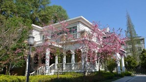Un edificio a due piani con un balcone e un portico, circondato da alberi e un cielo sereno.