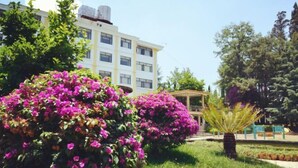 Un edificio con facciata bianca e numerose finestre, circondato da un lussureggiante verde e vivaci fiori rosa.