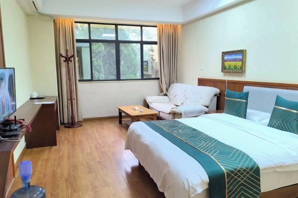 Een hotelkamer met een bed, een stoel, een klein tafeltje, een televisie en een raam met gordijnen.