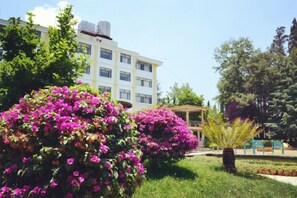 A building with a garden featuring pink flowers and a palm tree. - Yunnan Cadre Sanatorium (Anning)