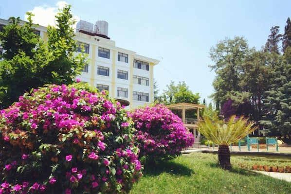 A building with a garden featuring pink flowers and a palm tree. - Yunnan Cadre Sanatorium (Anning)
