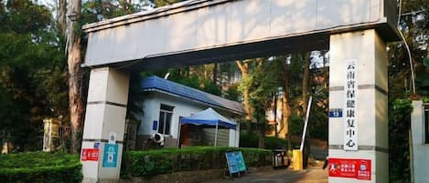 Une entrée couverte menant à un bâtiment, avec une enseigne dans une langue étrangère, un auvent bleu et un panneau indiquant un espace de stationnement.
