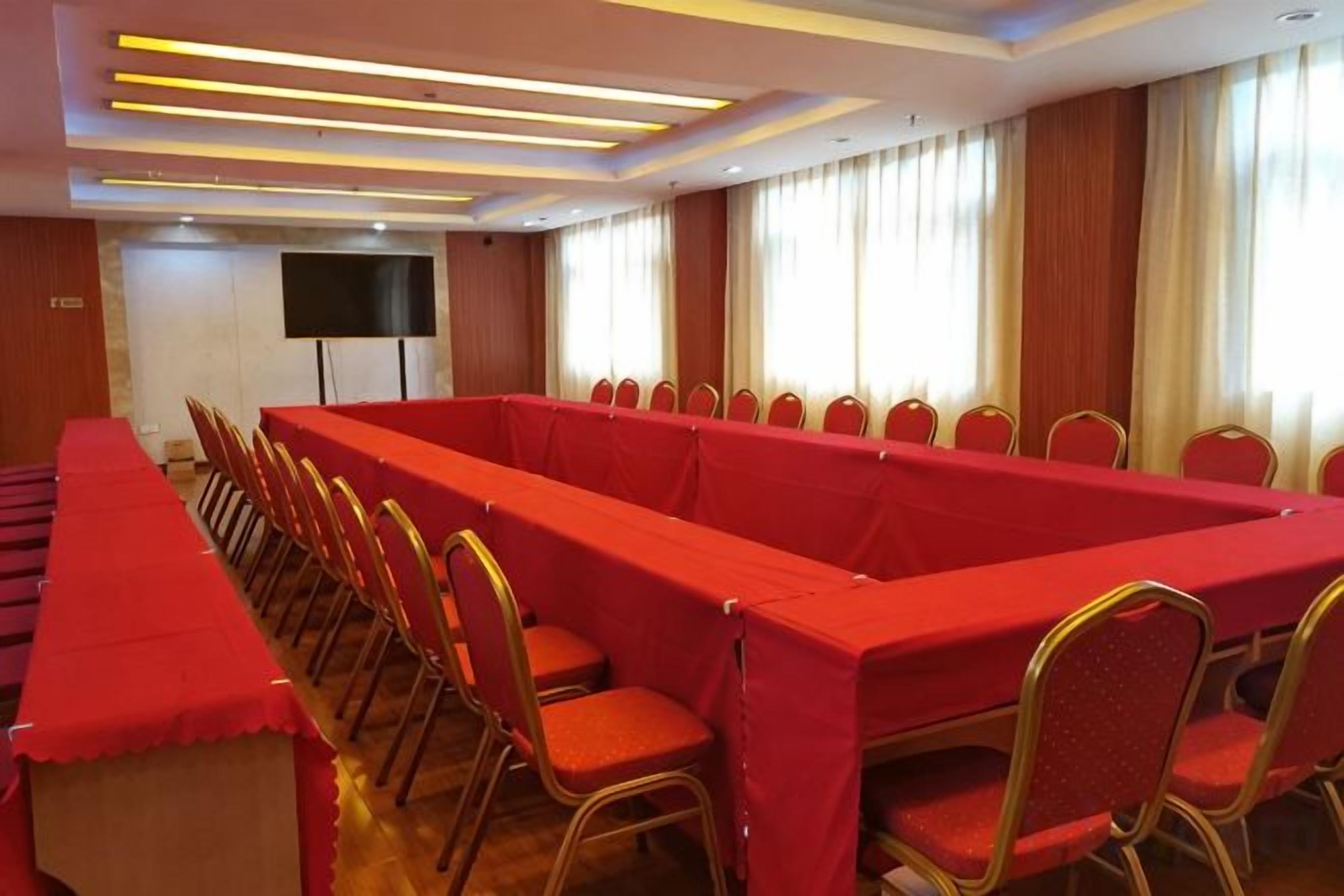 A conference room with a long table and chairs, a flat-screen TV, and a window with curtains.