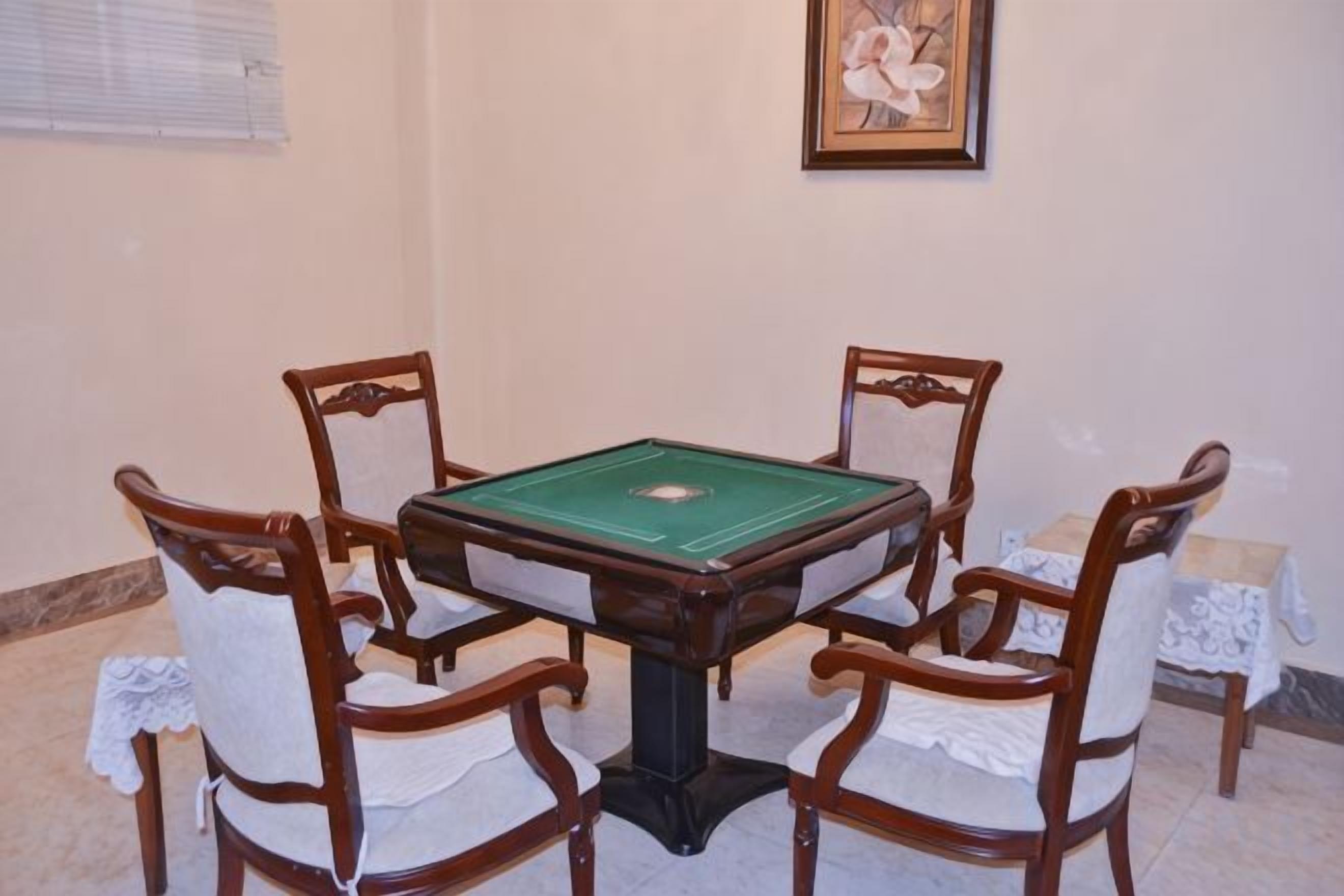 Una mesa de billar verde con cuatro sillas alrededor, en una habitación con un cuadro en la pared.