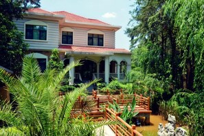 A two-story house with a red roof, surrounded by lush greenery and a wooden bridge. - Yunnan Cadre Sanatorium (Anning)