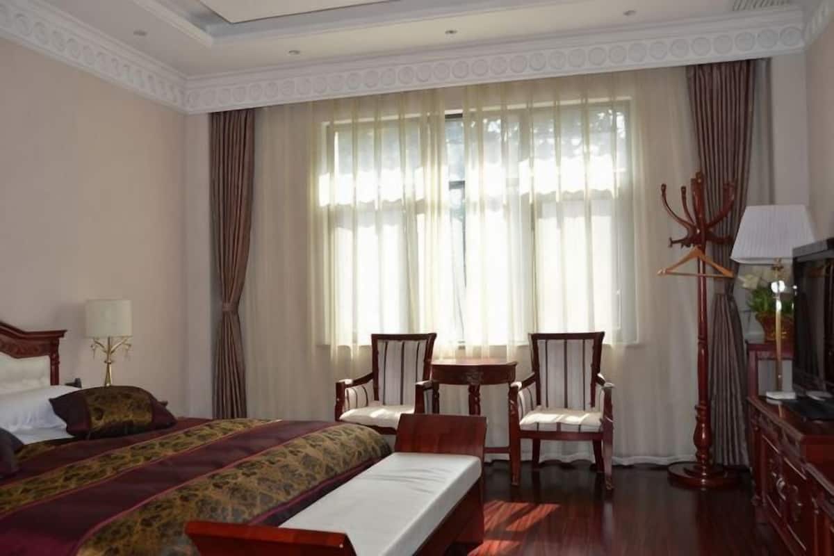 A hotel room with a bed, two chairs, a small table, a TV, and a lamp.