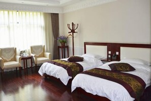 A hotel room with two beds, a sitting area with chairs, a small table, and a decorative item on the wall. - Yunnan Cadre Sanatorium (Anning)
