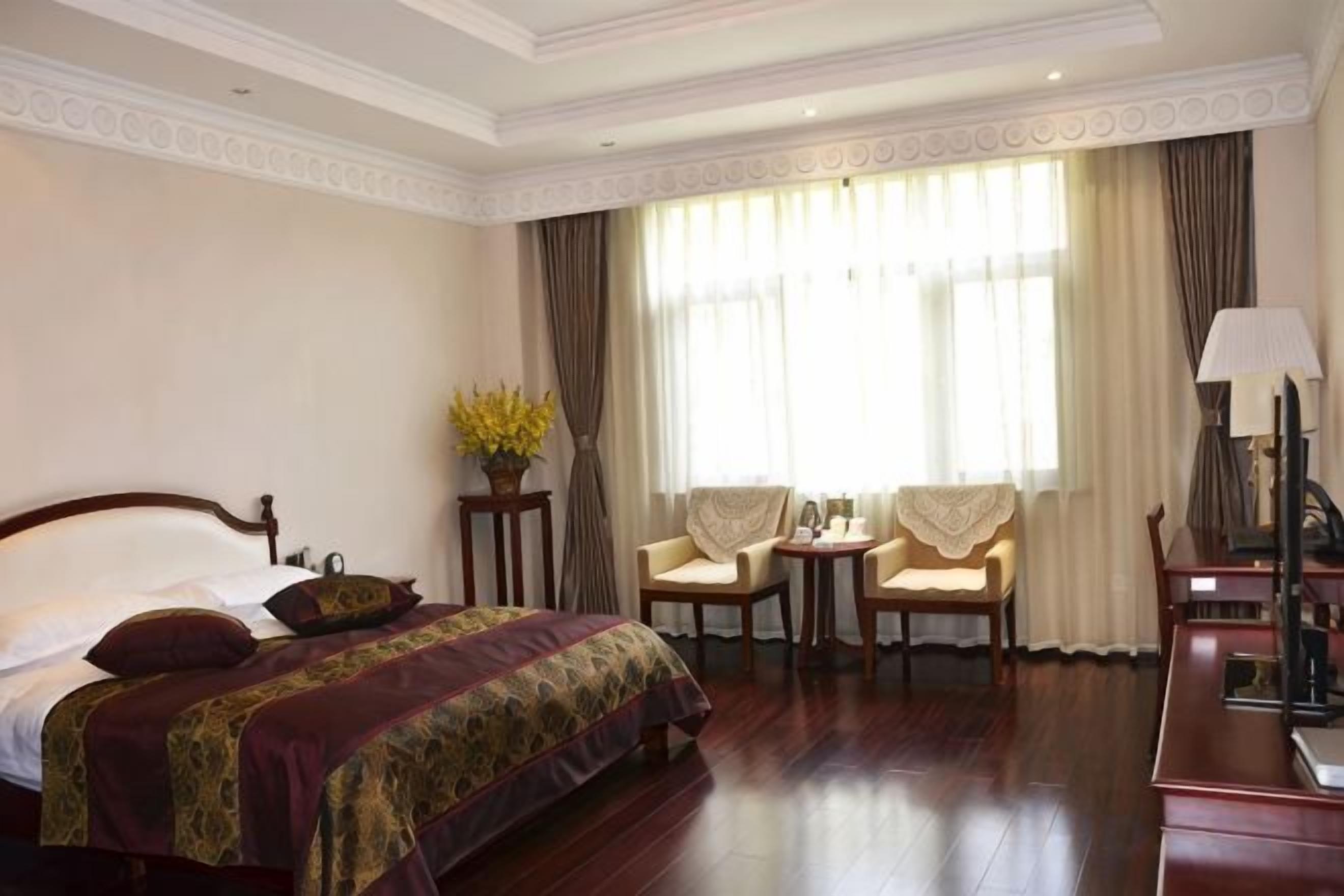 A hotel room with a large bed, two chairs, a small table, and a desk with a lamp.