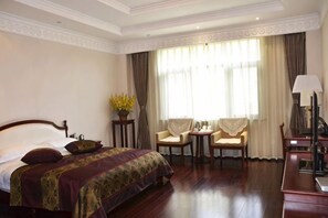 A hotel room with a large bed, two chairs, a small table, and a desk with a lamp. - Yunnan Cadre Sanatorium (Anning)