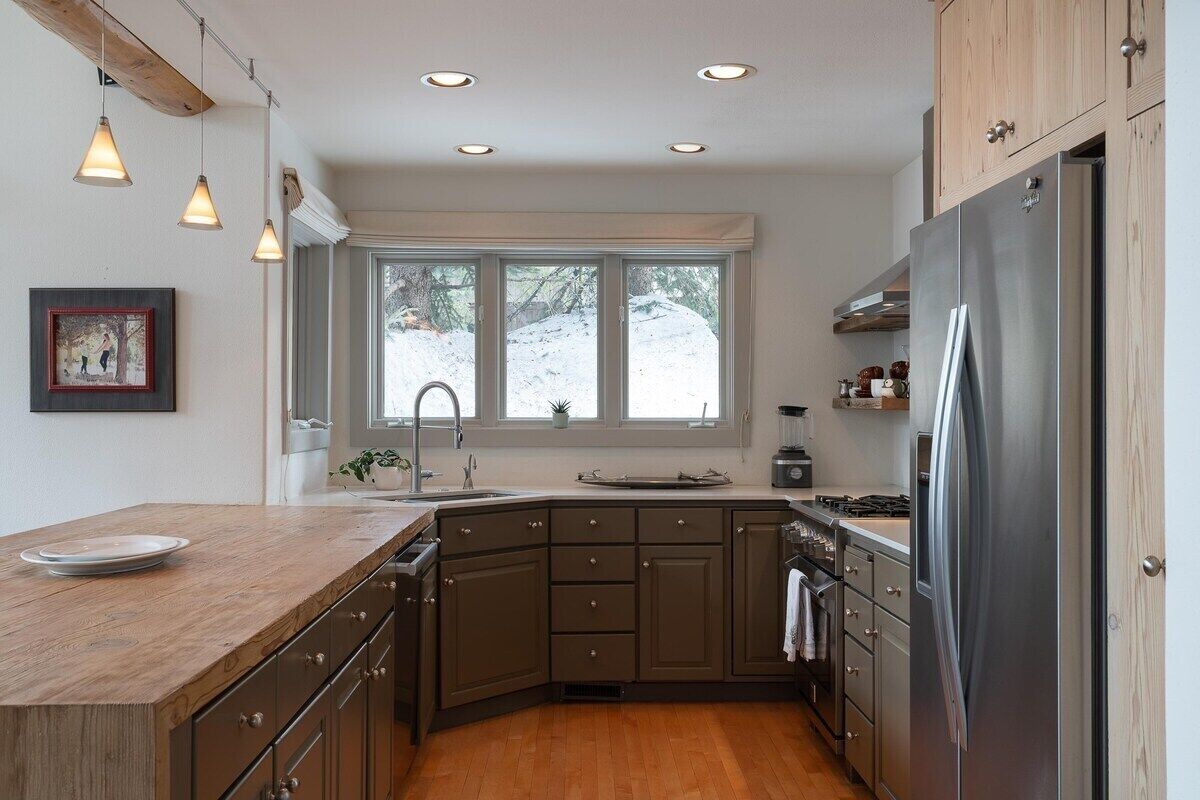 A modern kitchen with a wooden countertop, stainless steel appliances, and a large window providing natural light.