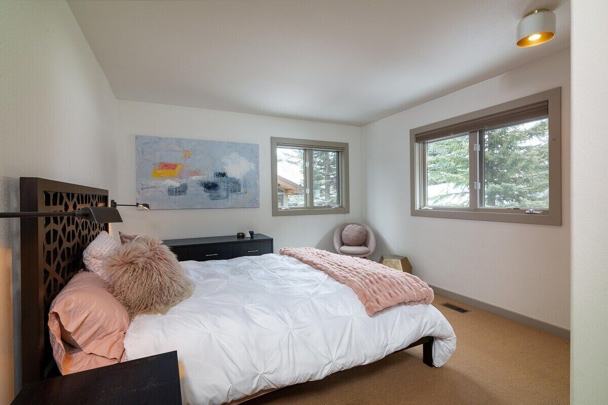 A bedroom with a bed, a desk, a chair, and two windows.