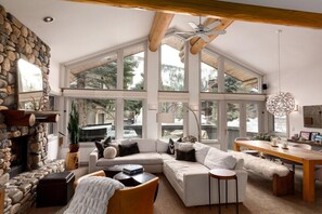 Un salon spacieux doté d’une cheminée en pierre, de grandes fenêtres, d’un plafond en bois et d’un coin salon confortable.
