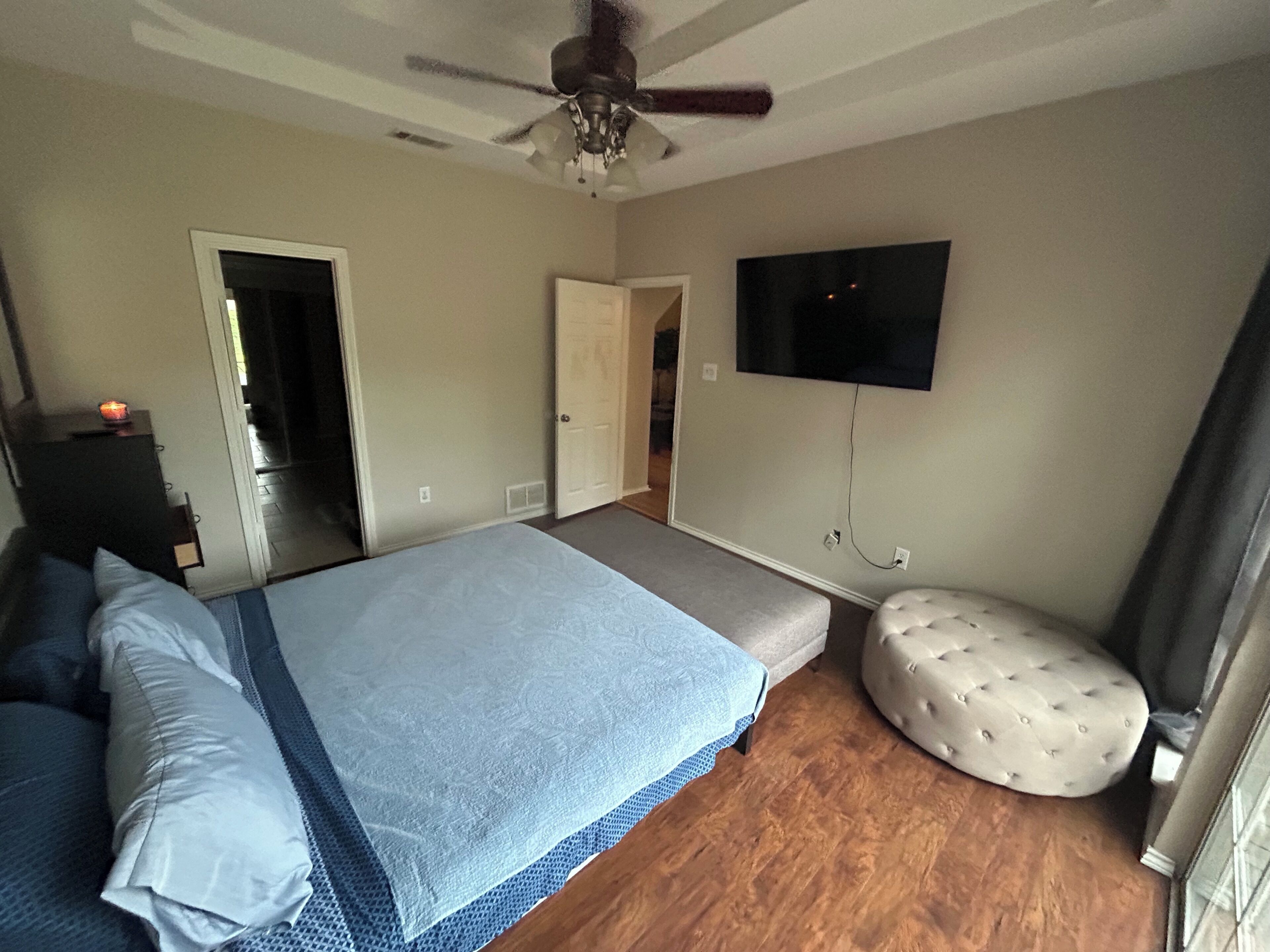 A bedroom with a bed, a ceiling fan, a television, and a door leading to another room.
