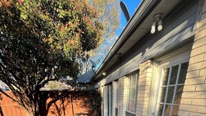 Un jardin avec un chemin de pierres menant à une terrasse, une clôture en bois et une maison équipée d’une antenne parabolique.