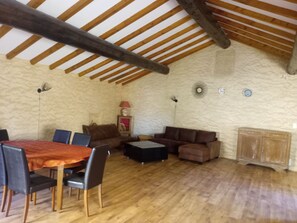 Une pièce spacieuse avec un plafond en bois, une table à manger avec des chaises, un canapé et un buffet.