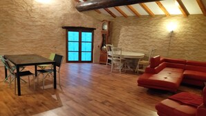 A room with a wooden floor, a dining table with chairs, a red sofa, and a large window with blue-tinted glass. - Proche Avignon Grande Maison calme en pierres avec cour intérieure,10 personnes (Saint Laurent des Arbres)