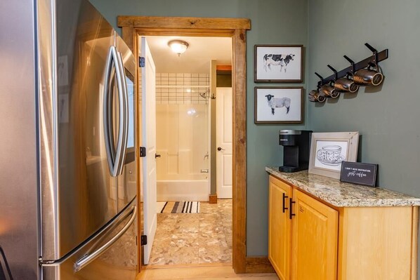 A kitchen with a stainless steel refrigerator, wooden cabinets, a granite countertop, and a coffee machine. - Watts Bar Tree House (Spring City)