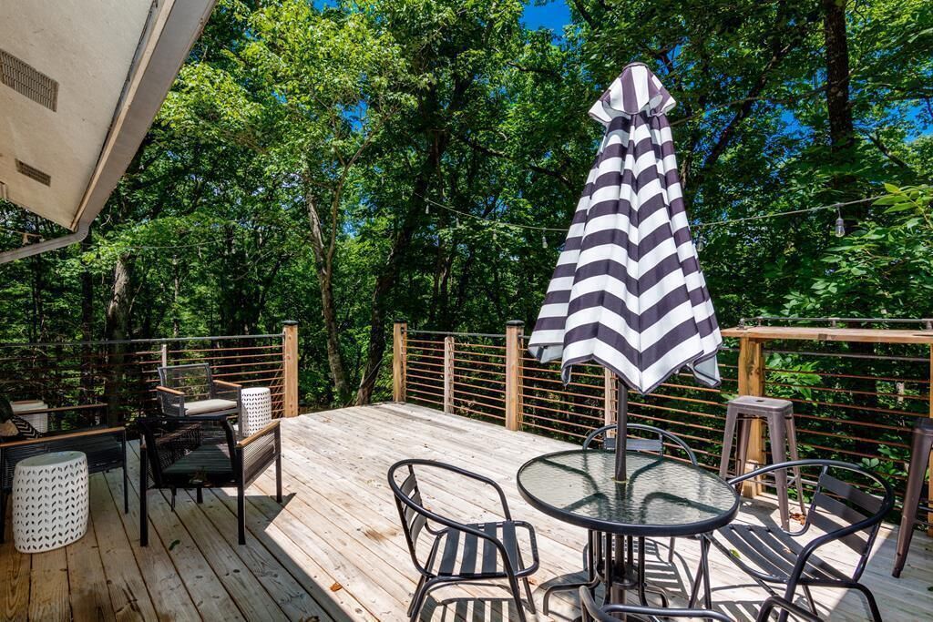 Eine Holzterrasse mit Gartenmöbeln, darunter ein runder Tisch und Stühle, sowie ein gestreifter Sonnenschirm.