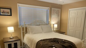A neatly arranged bedroom with a bed, two bedside tables, a window with blinds, a map on the wall, and a door. - Port Angeles History House (Port Angeles)