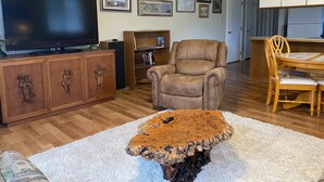 A living room with a television, wooden cabinet, armchair, coffee table, and framed pictures on the wall. - Port Angeles History House (Port Angeles)