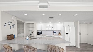 A modern kitchen with white cabinetry, a central island with bar stools, and a microwave.