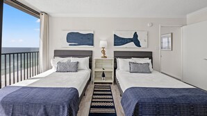 A hotel room with two beds, a nightstand, a lamp, artwork, a view of the ocean, and a balcony.