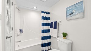 A bathroom with a white bathtub, a shower, and a toilet. There is a blue and white striped shower curtain, a towel rack with a towel, and a small plant on the toilet.
