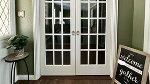 A foyer with a double door, a small table with a potted plant, and a welcome sign. - Beautiful Deck with Golf Course View/ Game Room/ Fire Pit (Conroe)