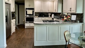 A modern kitchen with white cabinetry, stainless steel appliances, a granite countertop, and a glass dining table. - Beautiful Deck with Golf Course View/ Game Room/ Fire Pit (Conroe)