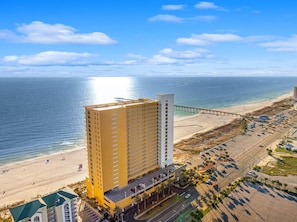 Un grand hôtel à plusieurs étages, avec un parking et une plage en arrière-plan.