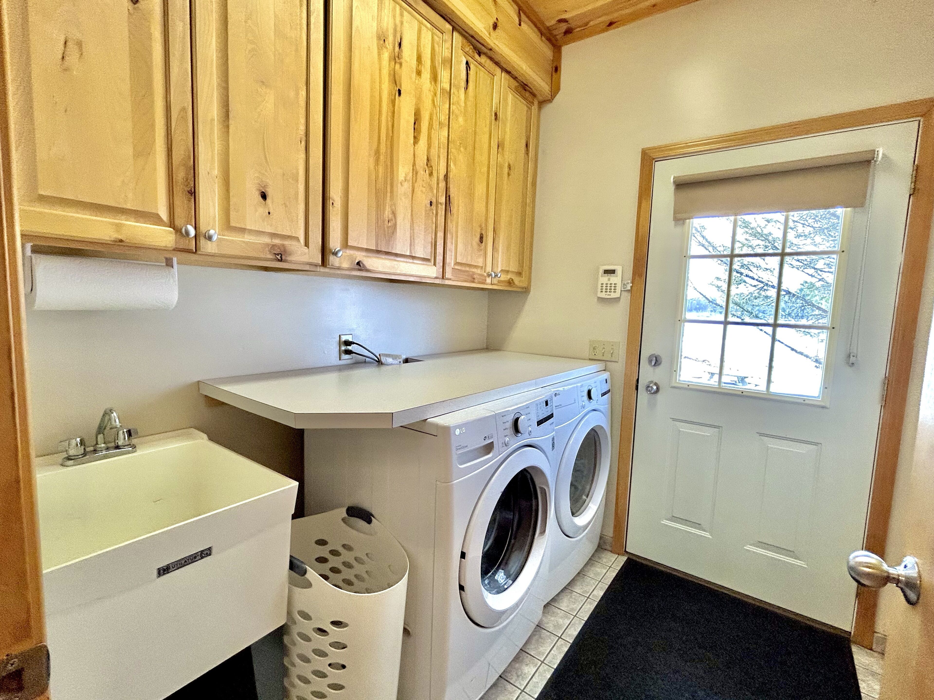 A laundry room with a washing machine, a sink, wooden cabinets, and a door with a window.